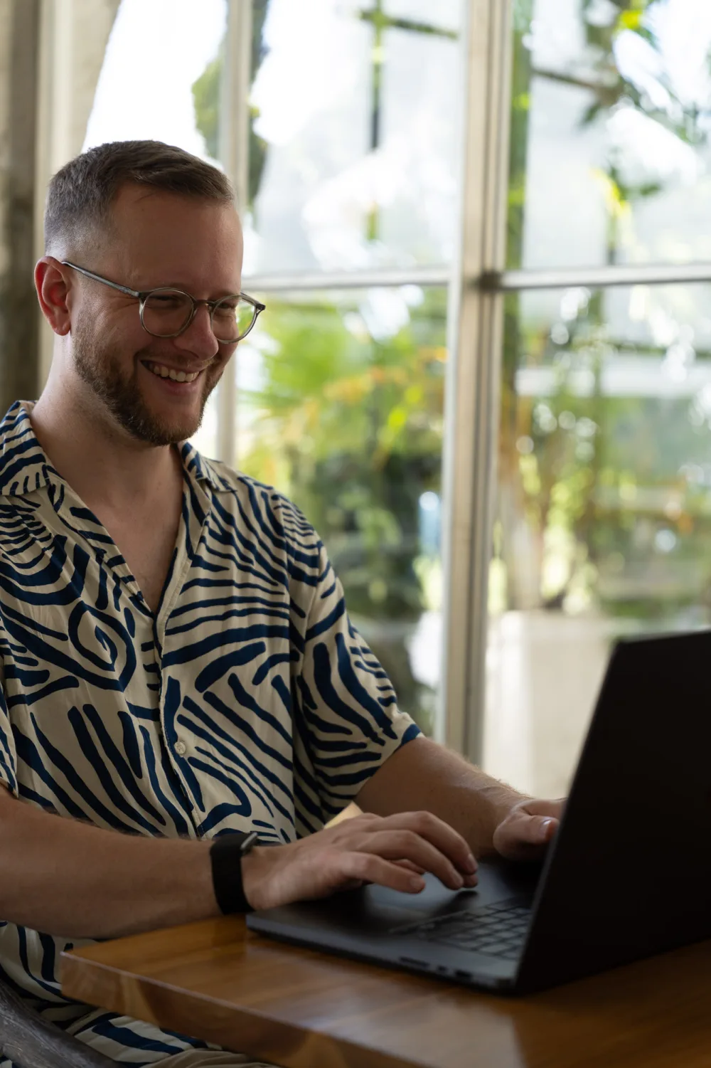 Felix arbeitet lächelnd am Laptop in einem Café auf Bali